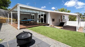 Et moderne hus med en overdækket terrasse, grill og en velplejet græsplæne.