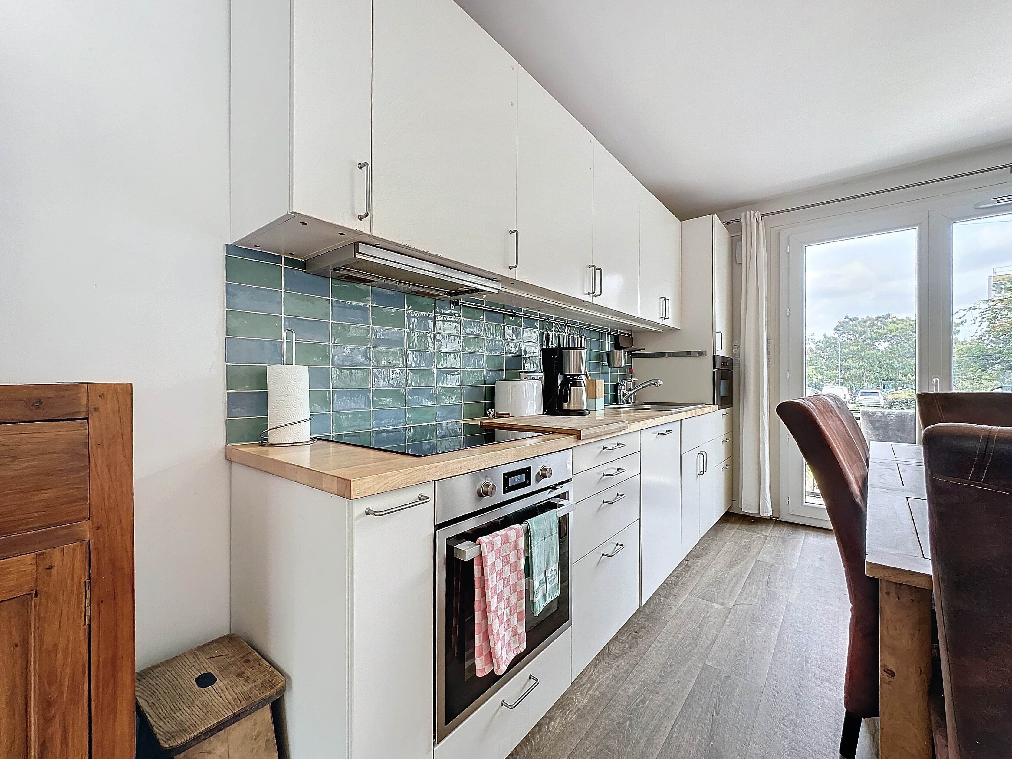 Una cocina moderna con armarios blancos, encimera de madera y vistas al exterior gracias a grandes ventanales.