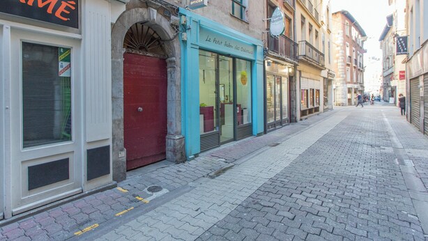 Eine Kopfsteinpflasterstraße mit Geschäften, darunter ein geschlossenes Restaurant und ein Boutique mit blauem Markisenvorhang.