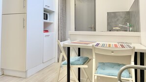 Eine kleine Küche mit weißen Schränken, einer Mikrowelle und einem Tisch mit farbenfroher Tischdecke.