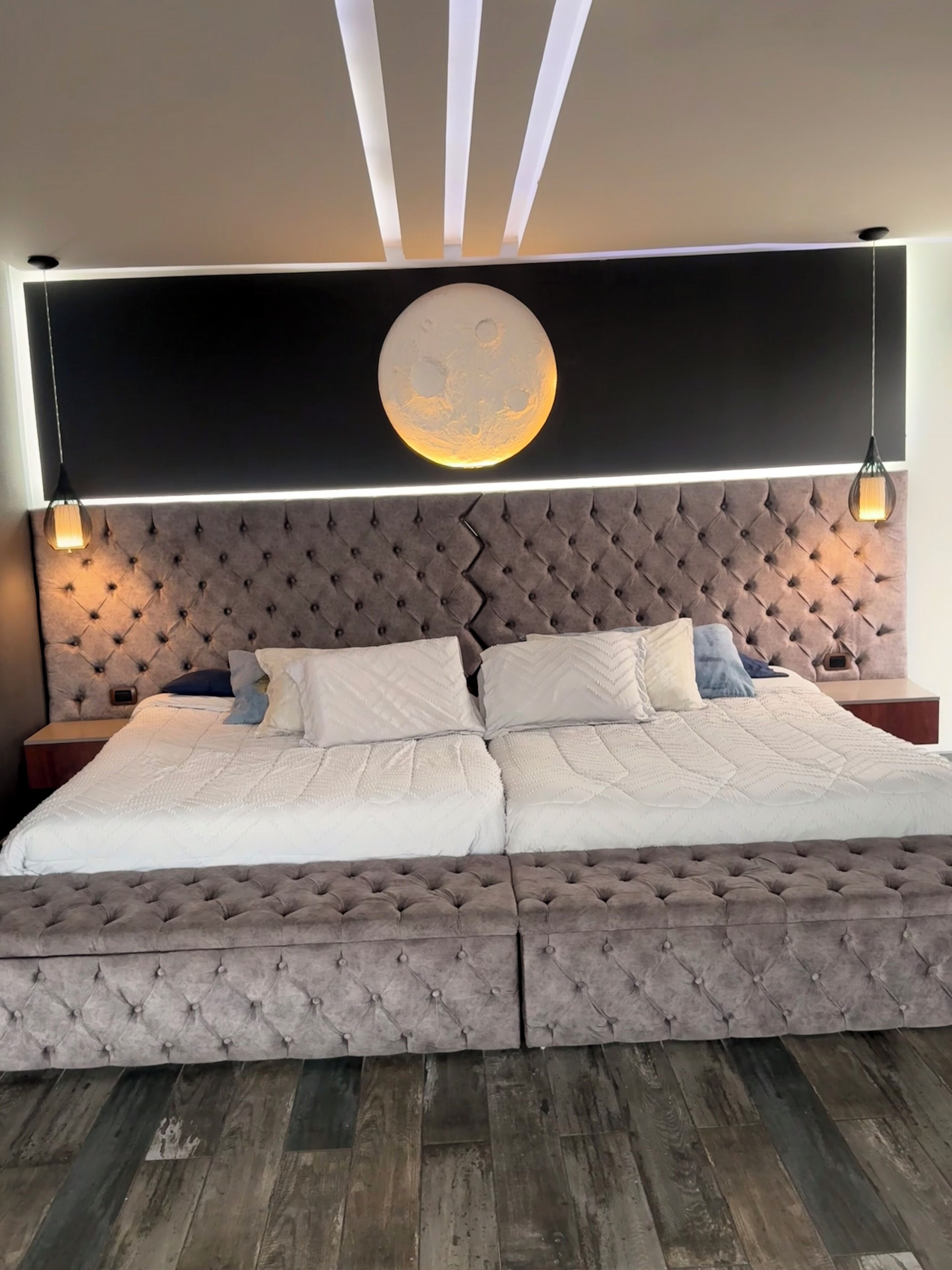Een groot bed met een geborduurde hoofdbord, twee nachtkastjes en een rond spiegel bevestigd aan de muur.