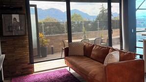 A modern living room with a leather sofa, a purple armchair, and a large window offering a view of mountains and a patio area. - MOVISTAR ARENA PENTHOUSE (Bogotá, D.C.)