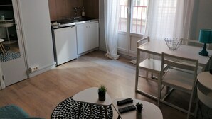 Eine moderne Küche mit weißen Schränken, einem Geschirrspüler und einem Spülbecken. Ein Essbereich mit Tisch und Stühlen, einer kleinen Topfpflanze und zwei Fernbedienungen auf dem Tisch.
