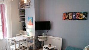 Ein modernes Wohnzimmer mit einem weißen Esstisch, weißen Stühlen, einem türkisfarbenen Sofa, einem an der Wand befestigten Fernseher und einem Schild mit der Aufschrift 'NEW YORK'.