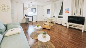 Una sala de estar moderna con sofá, mesa de centro, televisor, zona de comedor, cocina y un reloj en la pared.