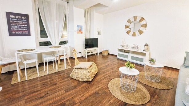 Una sala de estar moderna con piso de madera, muebles blancos, un televisor y objetos decorativos.