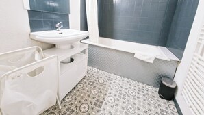 Un baño con un lavamanos blanco, paredes de azulejos oscuros, baldosas de suelo estampadas y una toalla blanca en el piso.