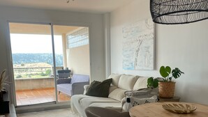 A modern living room with a sofa, chairs, a dining table, and a balcony with a view.