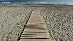 A wooden boardwalk leading to a beach with a clear sky and ocean in the background.