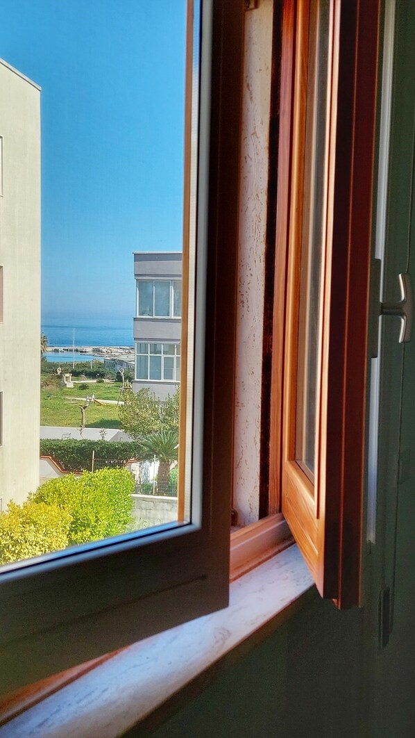 A window with a view of a modern building, a clear blue sky, and a body of water. - Mamma Anna's House - Otranto sea view (Otranto)