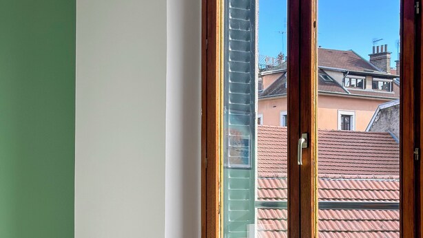 Ein Zimmer mit Fenster, einem kleinen Tisch und einem Blumentopf.