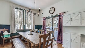 A dining area with a wooden table, benches, and chairs. There is a chandelier, a clock, and a view of trees through the windows. - 1 Mi to Big Boulder Mountain: Townhome W/gas Grill (Lake Harmony)