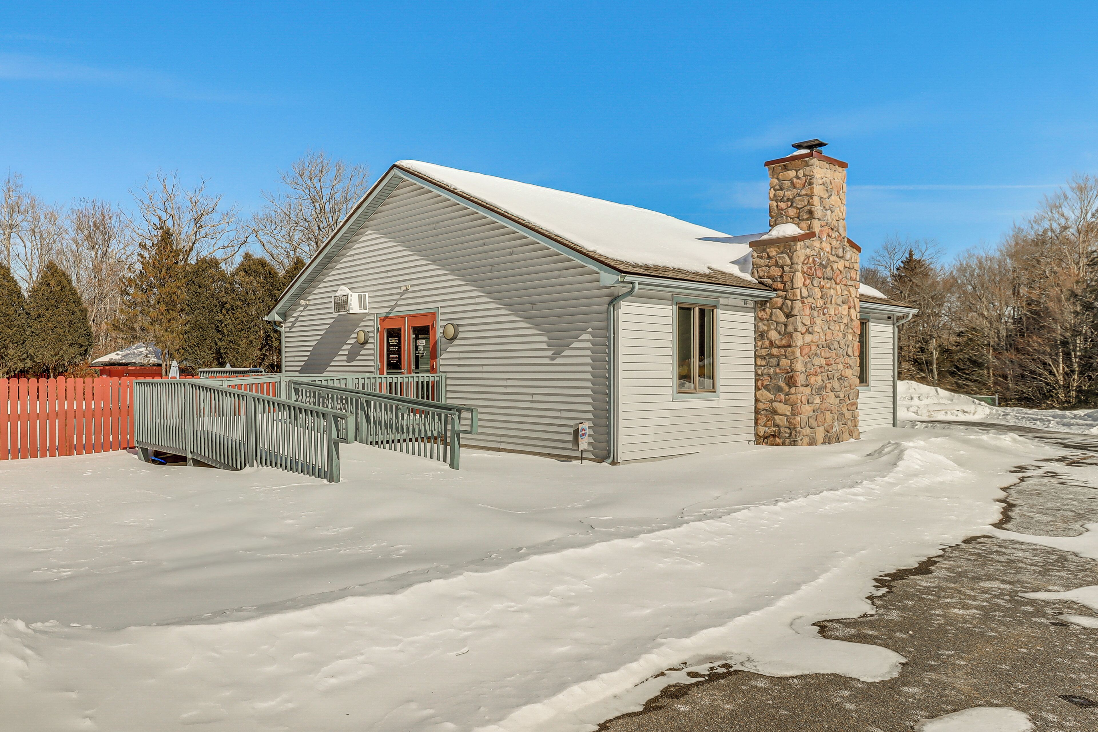 A single-story house with a stone chimney, a red door, and a covered porch.