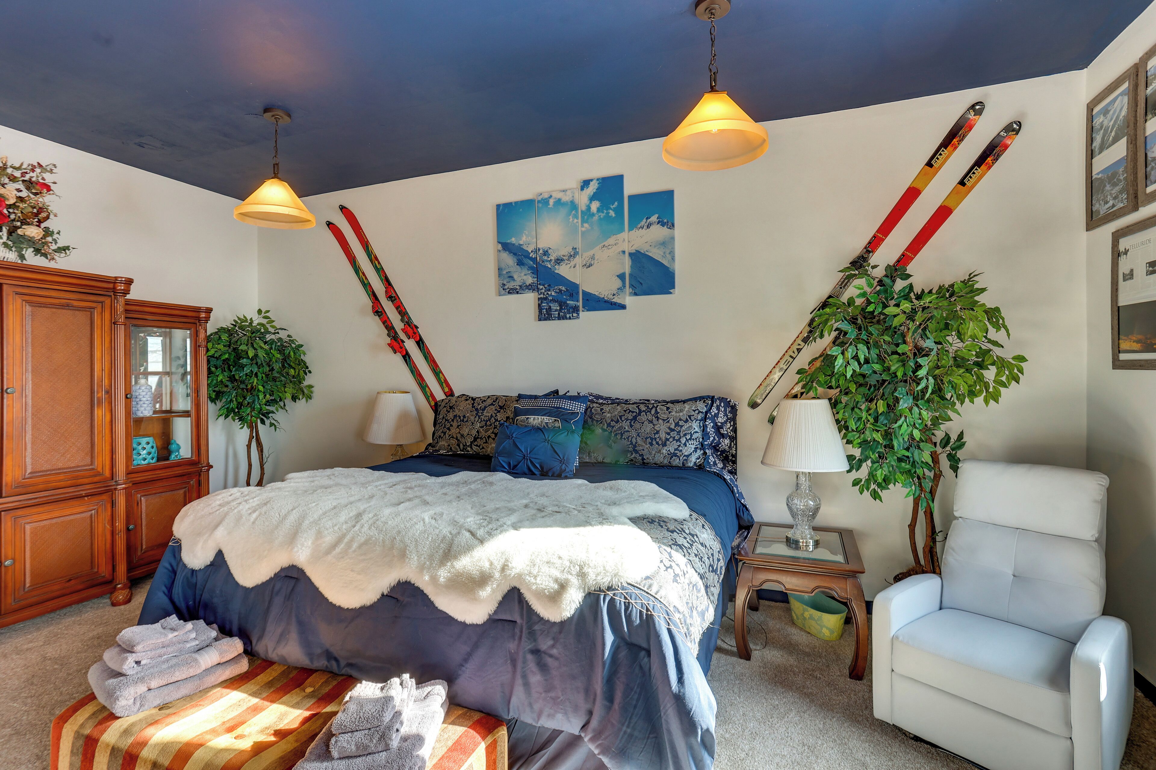 Slaapkamer met een groot bed, twee aan de muur bevestigde ski's, een houten kast, een stoel en een plant.