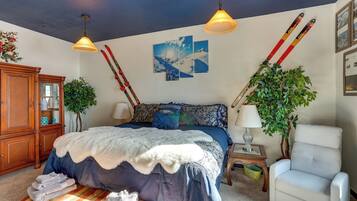 Slaapkamer met een groot bed, twee aan de muur bevestigde ski's, een houten kast, een stoel en een plant.