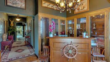 A lobby with a wooden reception desk featuring a ship's wheel, a chandelier, and framed artwork on the walls.