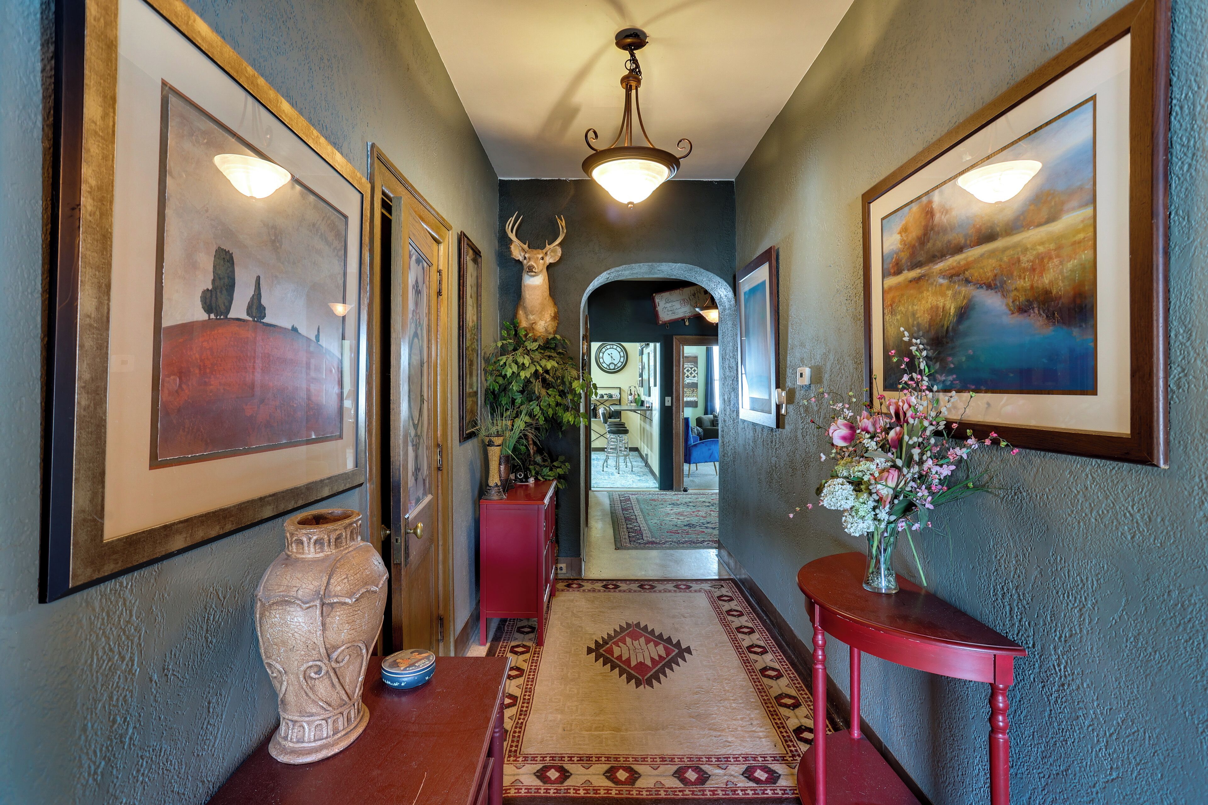 A hallway with framed artwork, a large vase, and a rug.