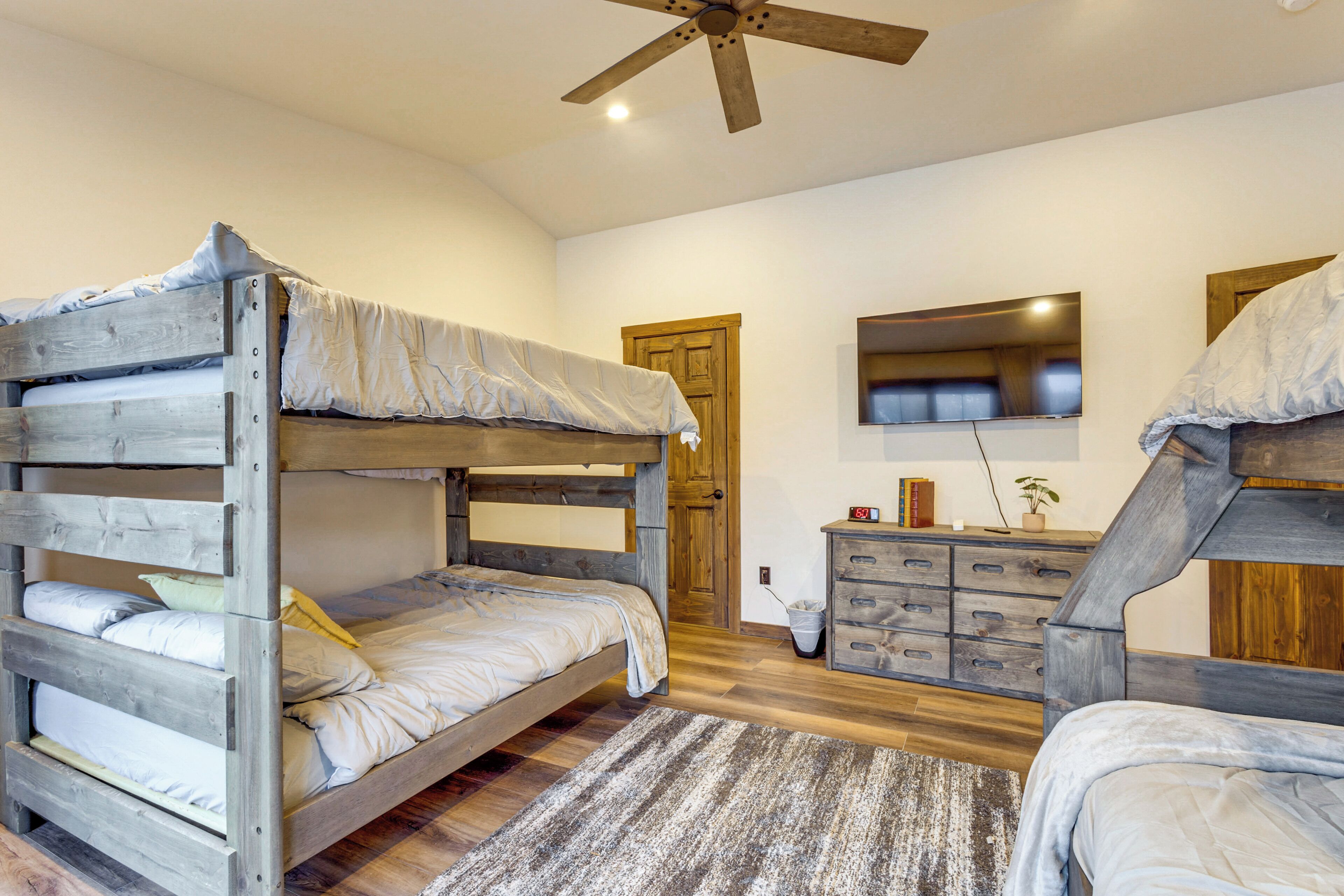 A bunk bed room with a wooden headboard, a dresser, and a ceiling fan.