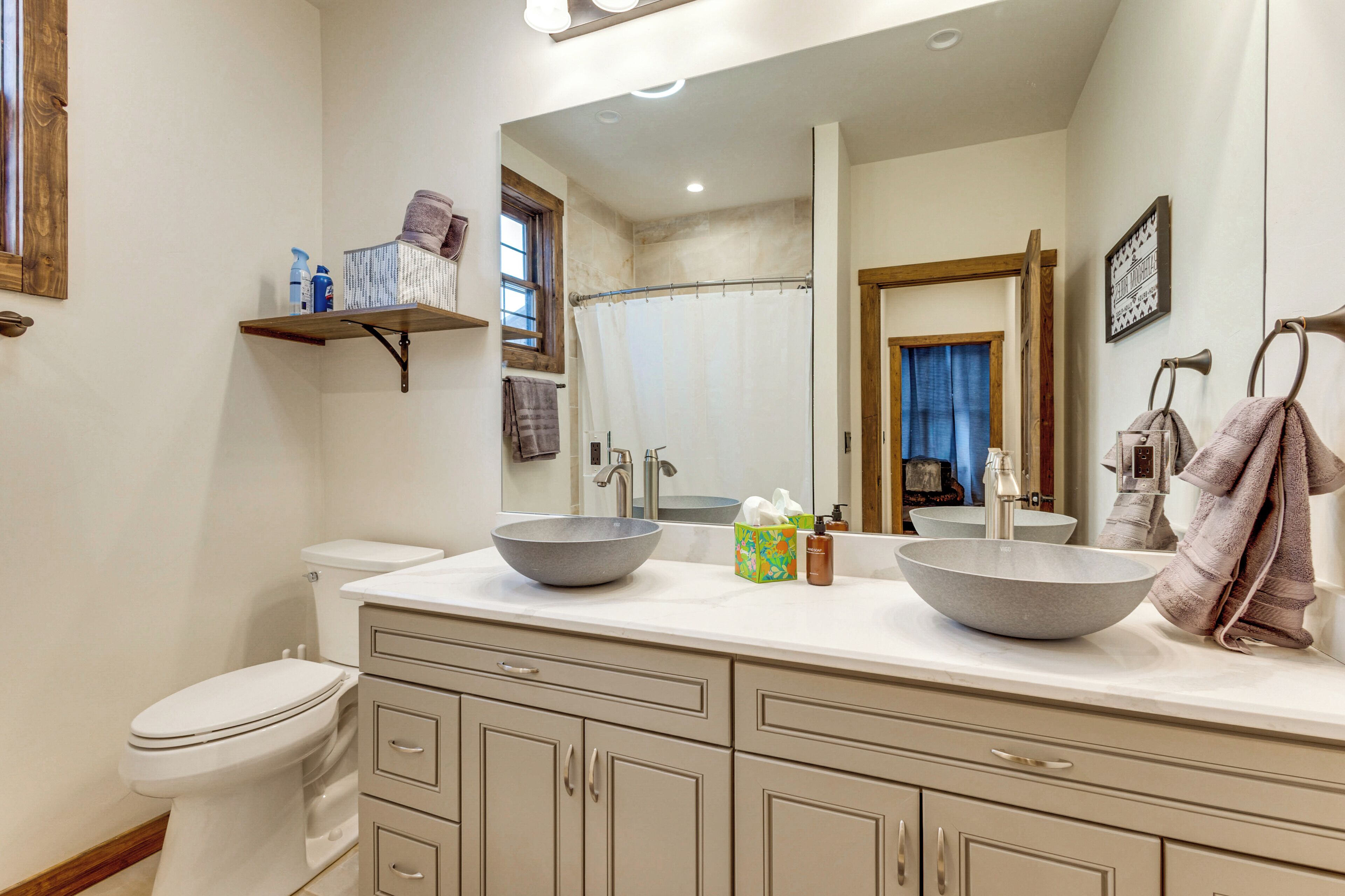 Une salle de bain avec un double lavabo, des toilettes, un grand miroir et un porte-serviettes.