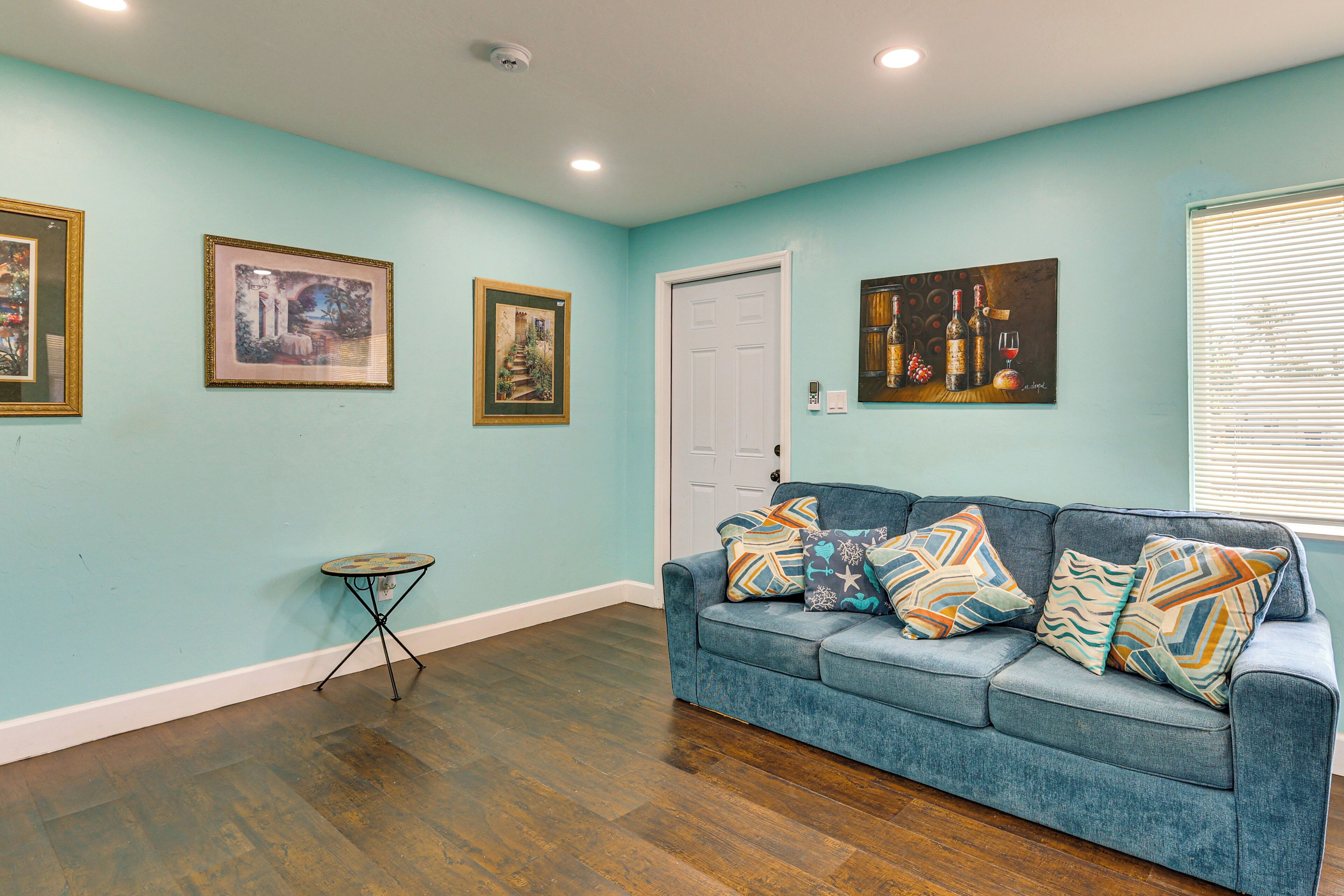 Une pièce aux murs de couleur turquoise, avec un canapé bleu orné de coussins à motifs, un plancher en bois et des œuvres d’art encadrées accrochées aux murs.