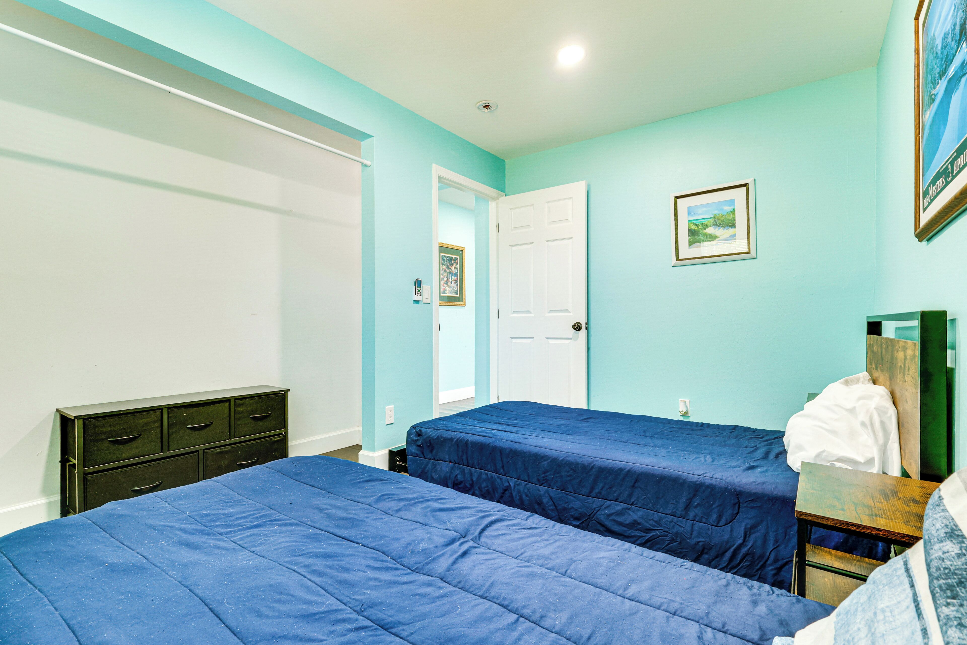 A bedroom with two beds, a dresser, and a door leading to another room.