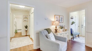A living room with a grey armchair, a small table with a lamp, and a blue chair. There is a hallway leading to another room. - 'petals & Pillows Getaway' 1 Mi to Dtwn Wendell! (Wendell)
