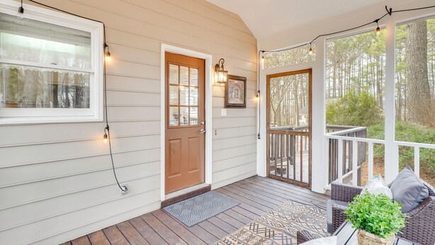 A covered porch with a wooden deck, a door, and a seating area with cushions and a plant. - 'petals & Pillows Getaway' 1 Mi to Dtwn Wendell! (Wendell)