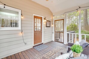 A covered porch with a wooden deck, a door, and a seating area with cushions and a plant. - 'petals & Pillows Getaway' 1 Mi to Dtwn Wendell! (Wendell)