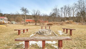Ein Picknickplatz mit Bänken und einer Feuerstelle im Zentrum, umgeben von trockenem Gras und Bäumen.
