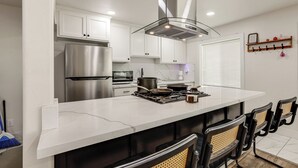 A modern kitchen with white cabinets, stainless steel appliances, and a central island with bar stools. - Under 1 Mi to Med Center! Stylish Home in Tulare (Tulare)