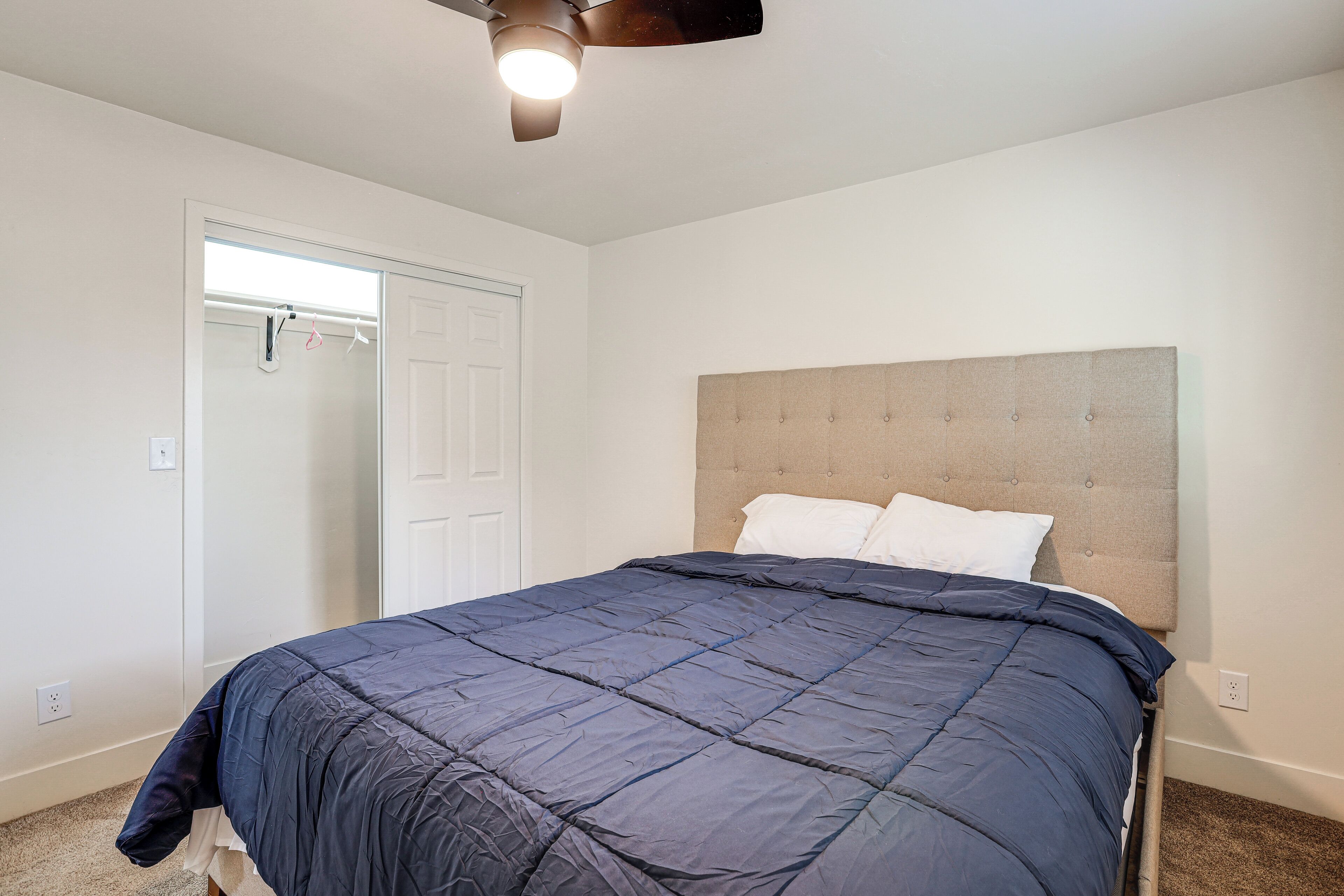 A bedroom with a bed, a ceiling fan, a door, and a closet.