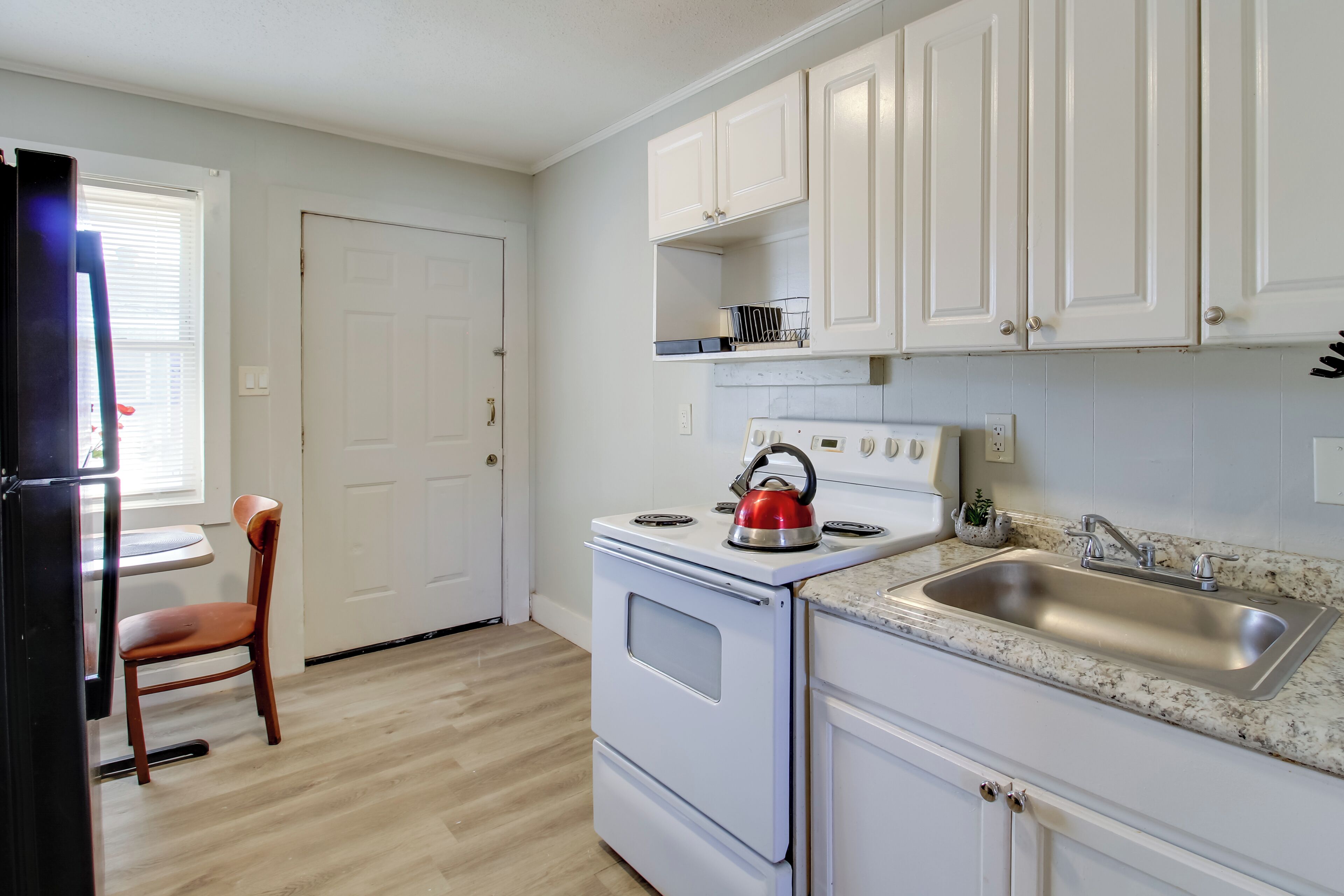 A kitchen with white cabinets, a stove, a sink, and a chair.