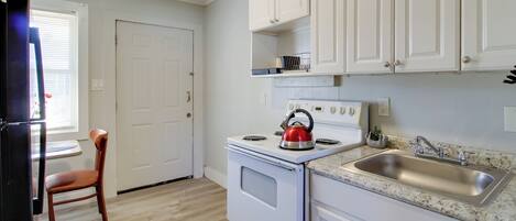 A kitchen with white cabinets, a stove, a sink, and a chair.