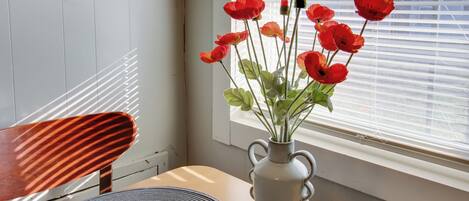 A vase with red flowers on a table near a window with blinds.