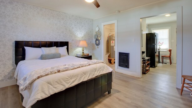 A bedroom with a bed, a ceiling fan, a nightstand with a lamp, and a fireplace. - Cozy Huntsville Studio Near Lowe Mill (Huntsville)