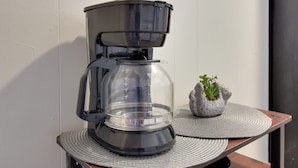 A coffee maker on a table with a placemat, a small potted plant, and a wall-mounted light fixture. - Cozy Huntsville Studio Near Lowe Mill (Huntsville)