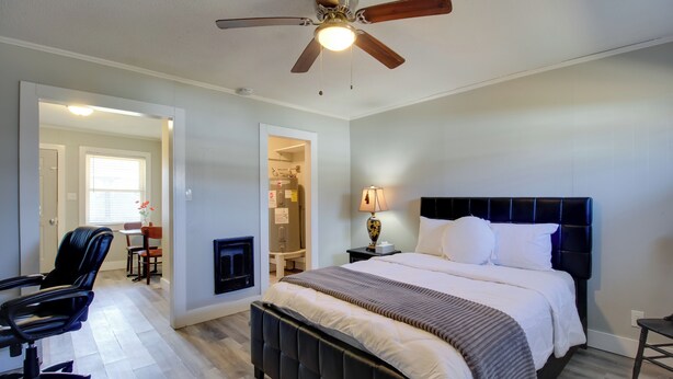 A bedroom with a bed, a desk, a chair, a ceiling fan, and a fireplace. - Huntsville Studio w/ Workspace Near Downtown (Huntsville)