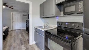 A kitchen with grey cabinets, a black microwave, a stove, and a dishwasher. - Huntsville Studio w/ Workspace Near Downtown (Huntsville)