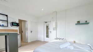 A modern bedroom with a bed, a small kitchenette, a mirror, and a shelf with plants. - #IH - Le Victoria 4 💟 (Grenoble)