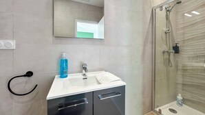 Un bagno moderno con box doccia in vetro, lavandino bianco e mobile contenitore nero.
