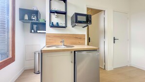 Una cucina compatta con lavandino, forno a microonde e frigorifero. Sono presenti scaffali con stoviglie e una porta che conduce in un'altra stanza.