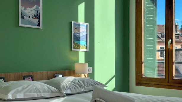 Camera d'albergo con un letto, cuscini, un comodino, una lampada e due poster alle pareti.