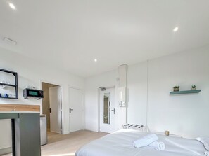 Un dormitorio moderno con cama, una kitchenette pequeña, un espejo y una repisa con plantas.