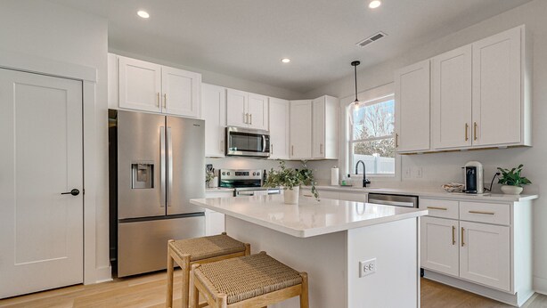 A modern kitchen with white cabinets, stainless steel appliances, and a central island with stools. - 4 Mi to Surf City Beaches! Family Coastal Retreat (Hampstead)