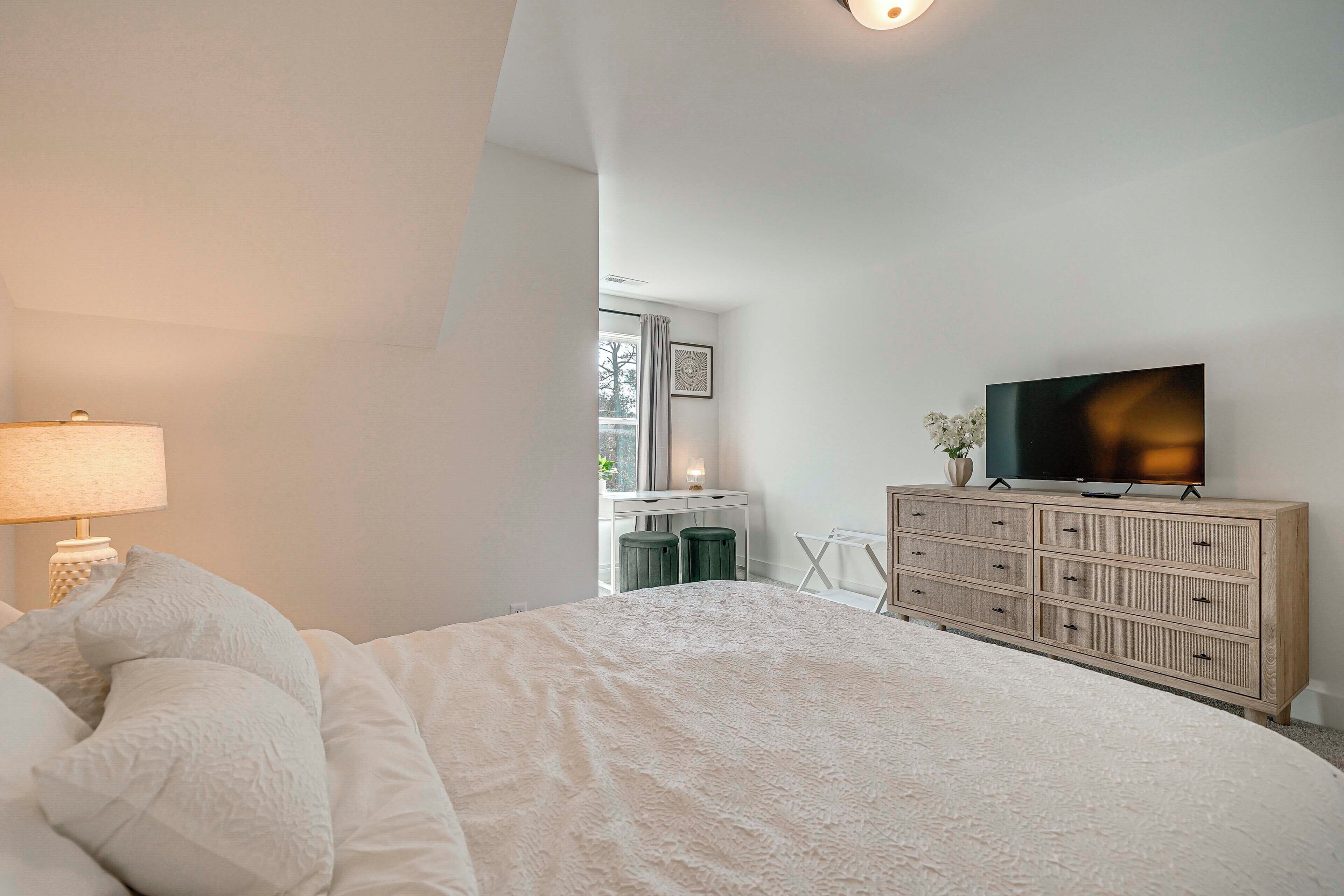 A bedroom with a bed, a dresser, a television, and a desk with a chair.