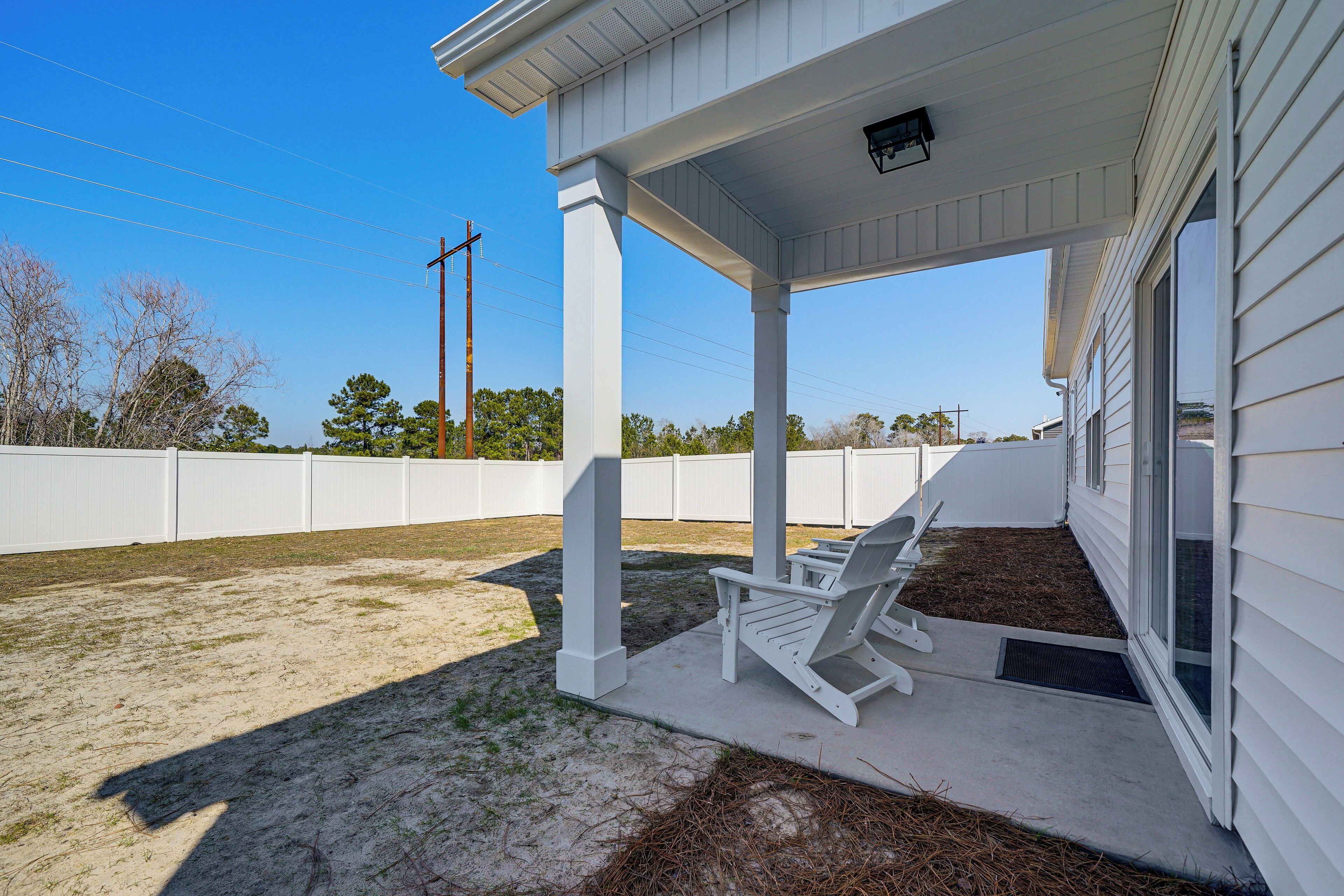 A covered patio area with two Adirondack chairs, a concrete floor, and a white fence in the background.