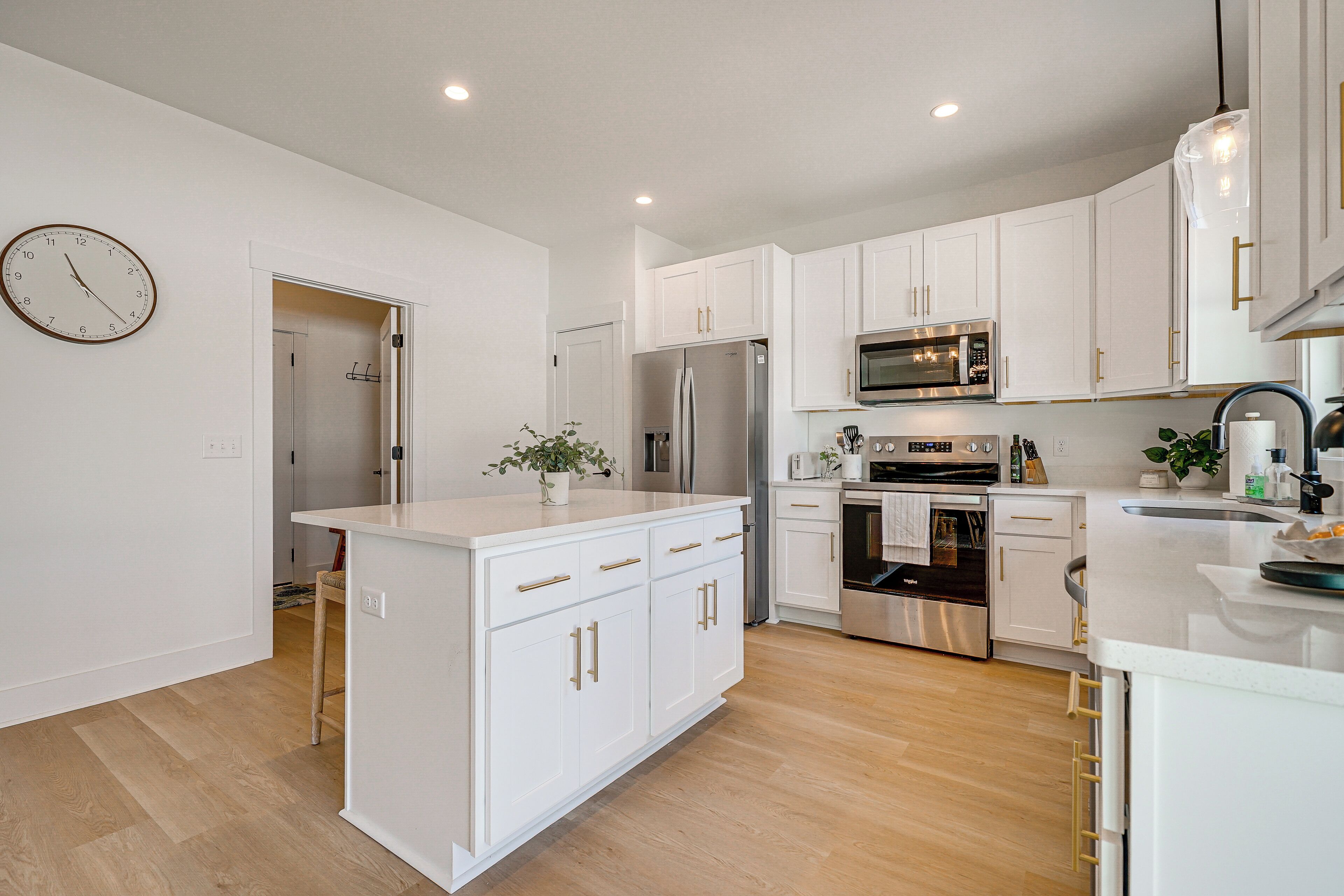 A modern kitchen with white cabinetry, stainless steel appliances, and a wooden floor.