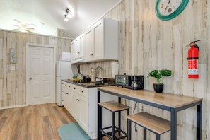 A kitchen with white cabinets, a microwave, a toaster, and a coffee maker. There is a fire extinguisher on the wall and a clock above the counter. - 4 Mi to Dtwn Picayune! Piney Woods Tiny Home (Picayune)