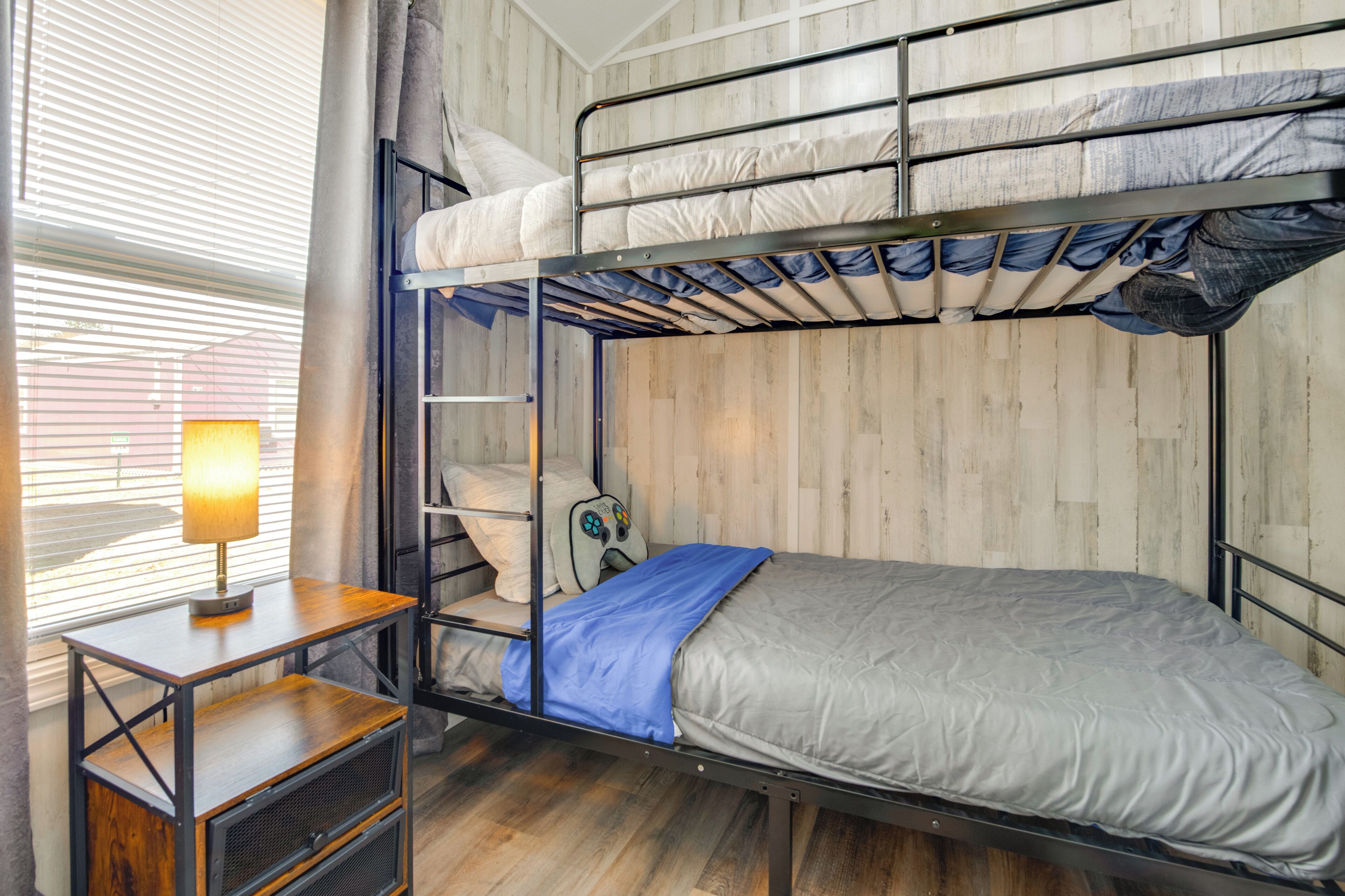 A bunk bed room with a desk and chair, a lamp, and a window with blinds.