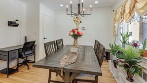 Uma sala de jantar com mesa de madeira, cadeiras, um candelabro e plantas em vasos.